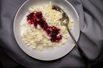 natural cottage cheese with raspberry jam in a white plate on a gray cloth