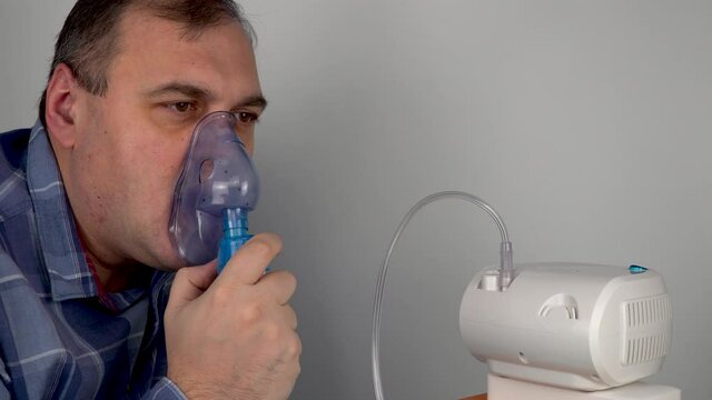 man holds a breathing mask and inhales. nebulizer and Oxygen Mask. spraying of a drug that is delivered to the patient through a mask or breathing tube. preventive medical procedures and treatment