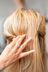 Back view of the female hand of hairdresser models a hairstyle of a young blonde woman in a hair salon