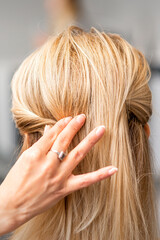 Fototapeta premium Back view of the female hand of hairdresser models a hairstyle of a young blonde woman in a hair salon