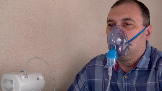 man holds a breathing mask and inhales. nebulizer and Oxygen Mask. spraying of a drug that is delivered to the patient through a mask or breathing tube. preventive medical procedures and treatment