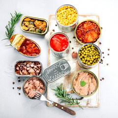 Various canned vegetables, fish and peas in aluminum cans on light gray background.