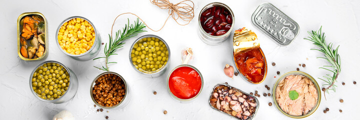 Various canned vegetables, fish and peas in aluminum cans on light gray background.