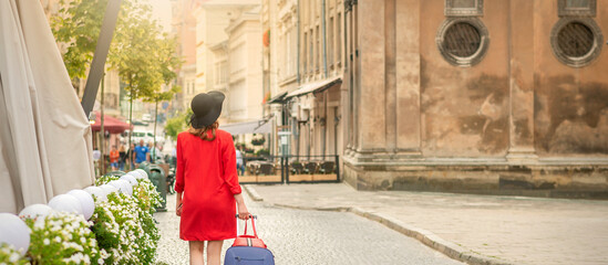 A young woman in a black hat with a suitcase walks on the European city street