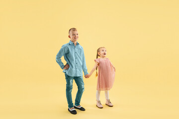 Astonished. Childhood and dream about big and famous future. Pretty boy and girl isolated on yellow studio background. Childhood, dreams, imagination, education, facial expression, emotions concept.