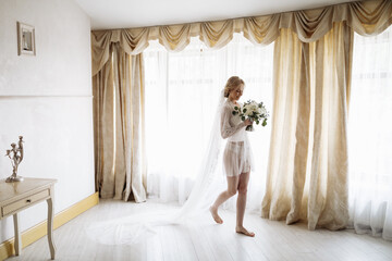 Portrait of a beautiful blonde bride in the interior. Morning young bride in a bathrobe. Smiling and cute girl stands.