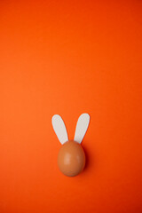 Aerial shot of an egg with rabbit ears on an orange background. Easter egg with bunny ears.