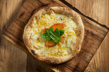 Delicious Italian pizza with crispy sides and 4 cheese filling with persimmon, spinach and honey. 4 cheese pizza on wood background