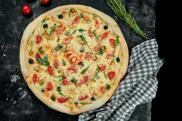 Appetizing italian pizza with shrimps, mussels, olives, tomatoes and rucola in a composition with ingredients on a black background. Top view