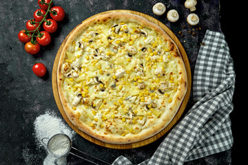 Appetizing hawaiian pizza with chicken, mushrooms, corn and pineapples in a composition with ingredients on a black background