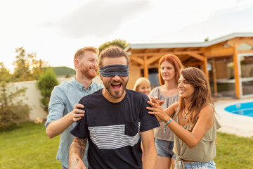 Friends having fun playing blind man's buff while at poolside summertime outdoor party