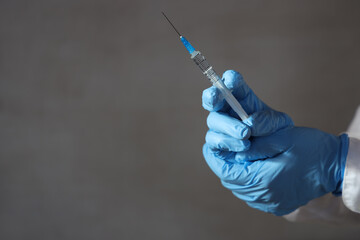 Doctor's hands in medical gloves hold a syringe for revaccination against omicron strain on gray background.
