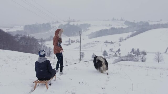 Kids playing and pushing sled with dog in winter 