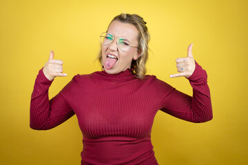 Young caucasian woman wearing casual red t-shirt over yellow background shouting with crazy expression doing rock symbol with hands up