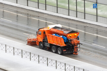 Snowplow Gritter is driving on the side of a road covered with a thin layer of ice.
