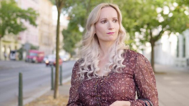 A middle-aged Caucasian woman thinks about something in an urban area - a city street with a road in the blurry background