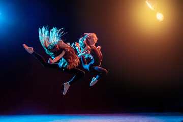 two ballet girls in tight-fitting costumes jumping on black background with their long hair down,...