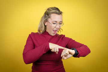 Young caucasian woman wearing casual red t-shirt over yellow background surprised and pointing his...