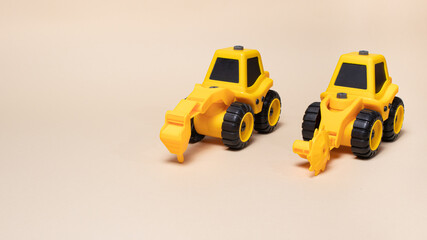 Two yellow construction tractors on a light beige background. Cars for children and toy store