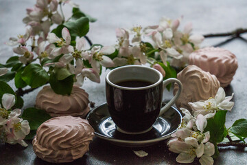 Delicious delicate white-pink marshmallows along with a blossoming apple tree branch and a cup of coffee.