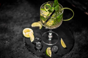 Cocktail Mojito drink with peppermint citrus lime slices in crystal glass on a dark black gray background bar