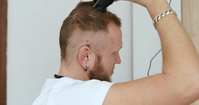 Handsome man in white t-shirts cutting hair personally himself with machine trimmer, clipper at home. Self Care during quarantine isolation. Stay home, hairdresser