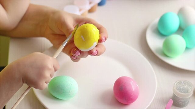 mother hand  holds egg and child using paintrush coloring it with yellow paint  happy easter decoration close up