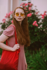 Young beautiful red-haired long-haired woman in a summer pink dress walks through the streets of a summer city.