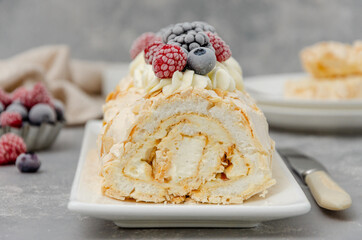Meringue roll Pavlova cake with cream and raspberries, blackberries and blueberries on top on a gray background. Copy space.