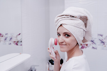 Portrait of a young woman with bad skin removing makeup with cleansing brush, device for household...