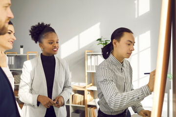 Fototapeta premium Team of multiethnic office workers attending useful workshop. Experienced business coach meeting with group of young people, giving teamwork advice, sharing professional knowledge and expertise