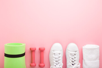 Female fitness training accessories. White sport shoes, dumbbells, green foam mat and towel on...