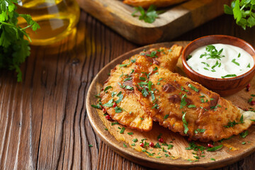 Traditional cheebureki, served on a wooden plate with sauce.