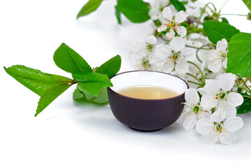 Green tea in a ceramic cup with twigs of blossoming cherry tree isolated on a white background. 