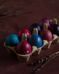 Colored Easter eggs in carton box on dark purple background