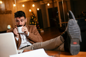 Young businessman using laptop and drinking coffee in his office. Handsome man on coffee break