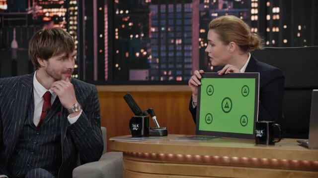 FIXED Attractive late-night talk show female host showing a green board with tracking points to handome celebrity guest in a studio. TV broadcast style show. Shot with RED cinema camera