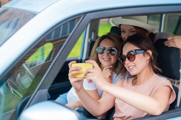 Three happy girlfriends go on a trip. Women are driving in a car and taking a selfie on a mobile phone