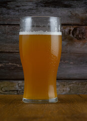 A glass of unfiltered beer with white foam on a wooden table