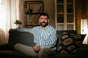 Fototapeta premium Young man at home. Man sitting in living room watching movie and drinking beer.