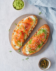Two open sandwich, toast with salmon, cream cheese, avocado, cucumber slices on white concrete table. Morning healthy breakfast with fish and cup of drink, top view, vertical