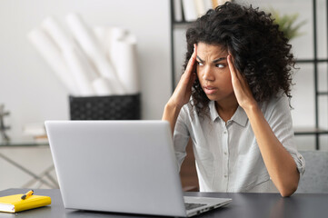 Young African American female office worker feeling stressed, annoyed from the office noise,...