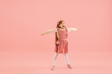 Crazy happy, astonished. Childhood, dream about big and famous future. Pretty longhair girl on coral studio background. Childhood, dreams, imagination, education, facial expression, emotions concept.