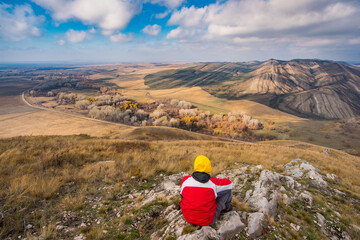 Fototapeta na wymiar a traveler sits on a hill and a small mountain in autumn and looks into the distance