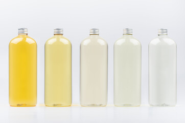 Assortment of plastic tall bottles with cosmetic essential oil of different pastel pale colors, silver cap mockup on white background, template.