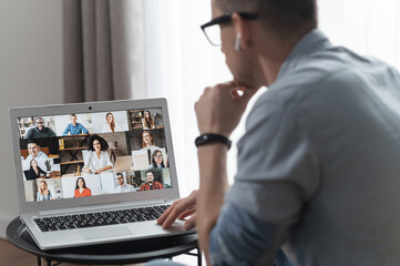 View from back above shoulder on the laptop with diverse employees, coworkers on the screen, video call, online meeting. App for video conference with many people together