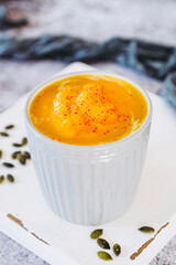 Soupe de courge au curry et baies roses dans un bol sur un fond couleur béton