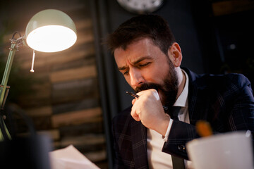 Exhausted businessman working on computer in the office. Tired man sitting at office desk drinking coffee..
