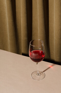 Vertical image.Glass of red wine on the brown table against folds of curtains