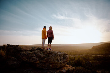 Rear view of young man and woman standing looking at beautiful sunrise on mountain cliff peak